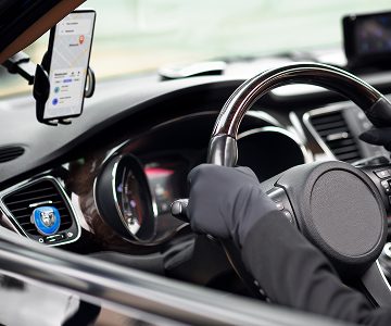 A view of a hand
            holding the steering wheel of a car, with a navigator shown on a
            phone screen.